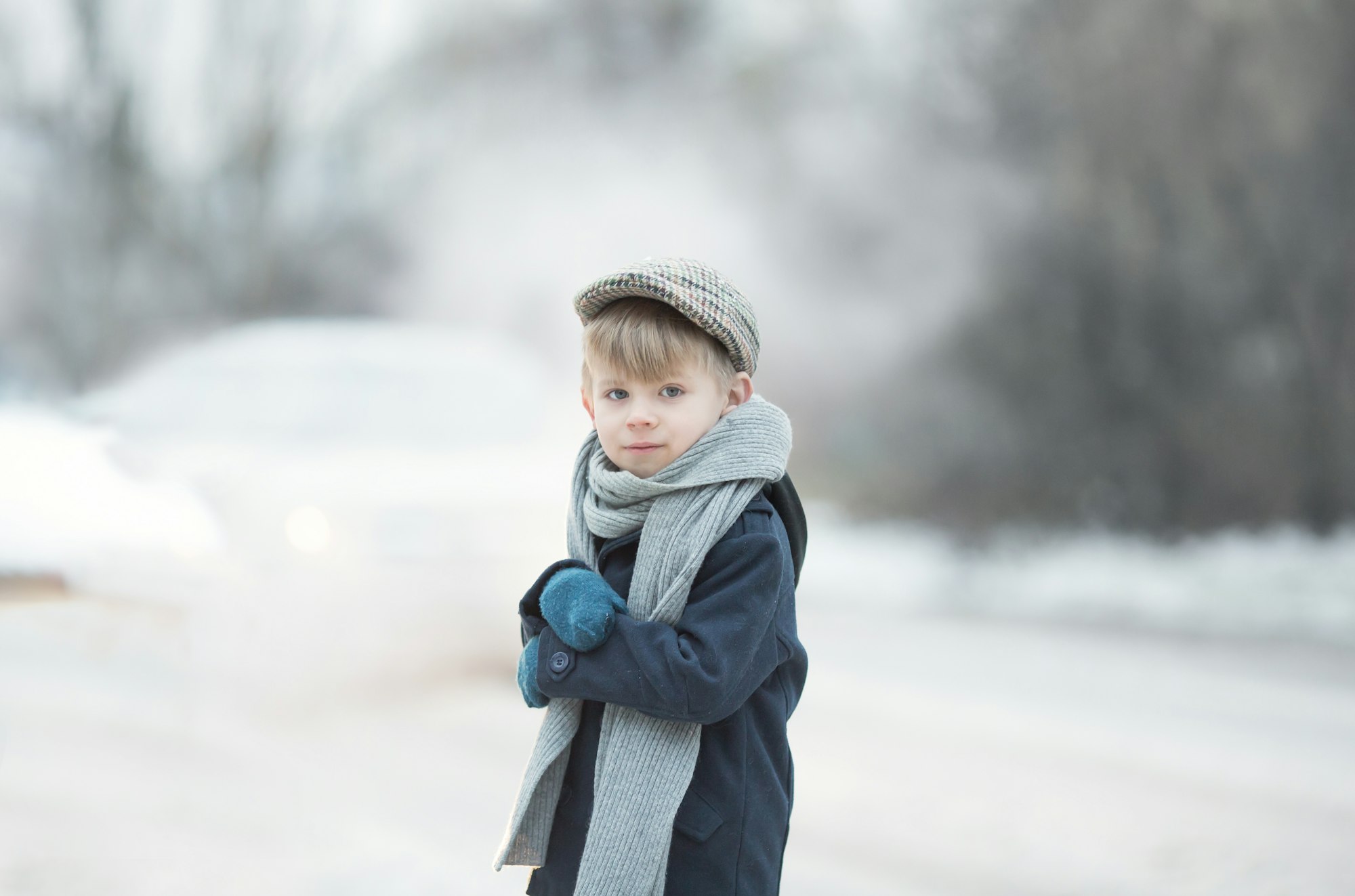 a boy in vintage clothes is standing by the road, he is cold, he is shivering,