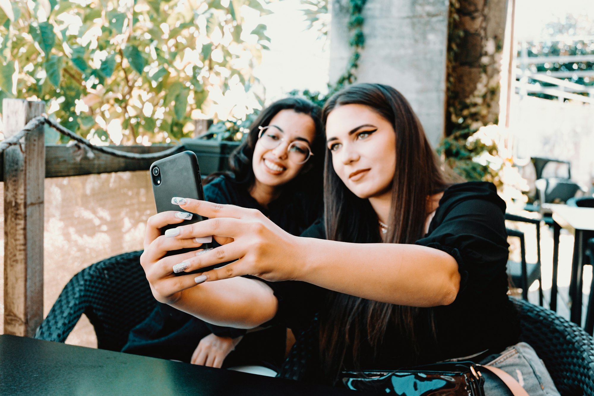 A couple of women taking a selfie with the focus put on the phone while they are both smiling