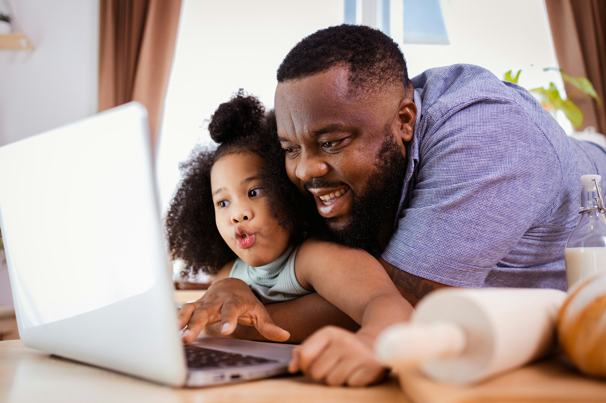 African American Dad teaches his little girl to make cookies by watching how to do it on laptop