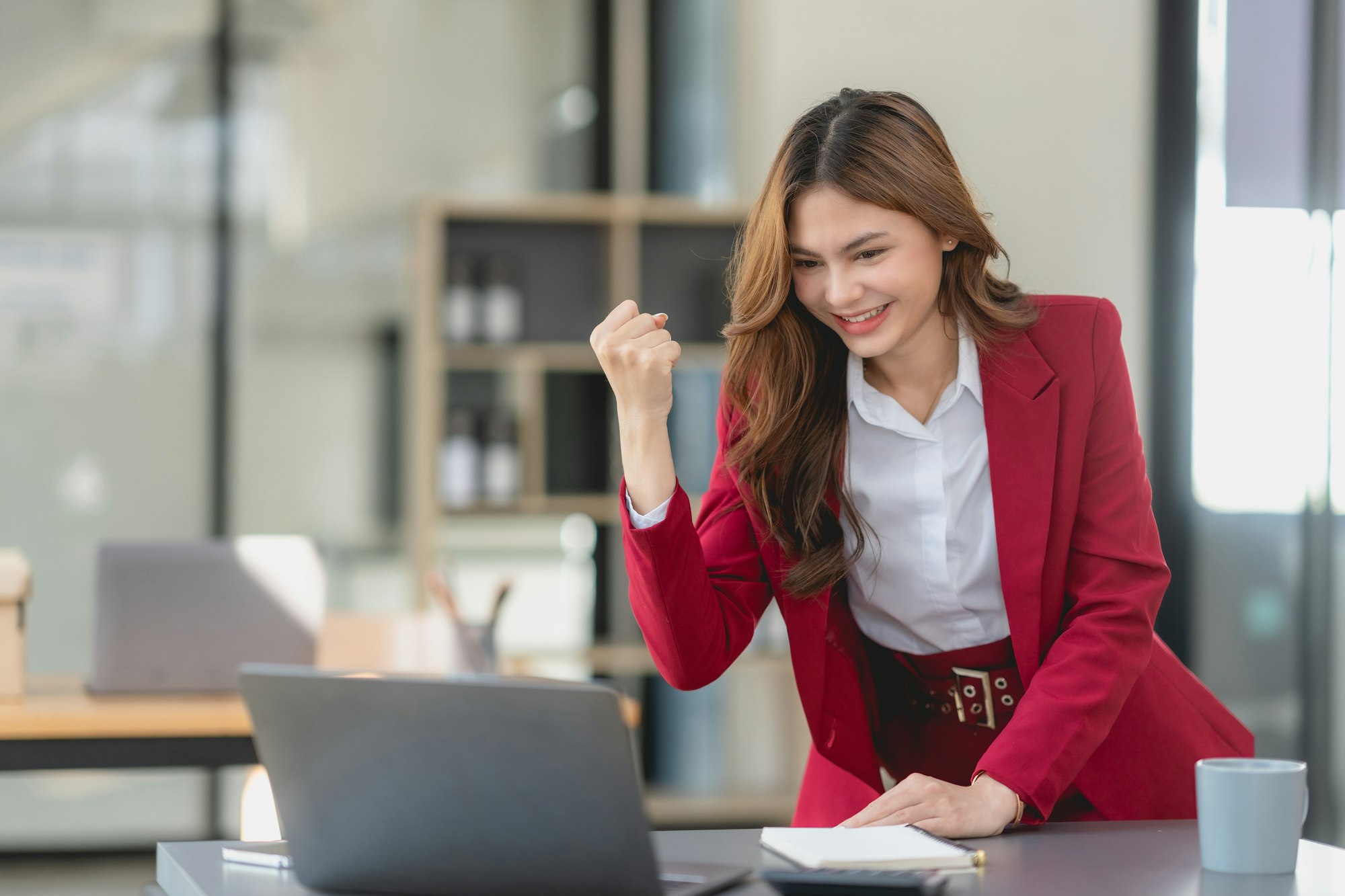 Excited cheerful business woman using laptop computer in the office, getting good news