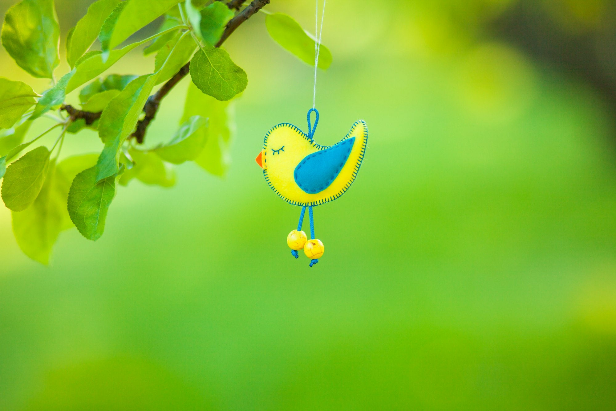 Felt bird on a green background, on an apple branch, ecology, needlework, with your own hands