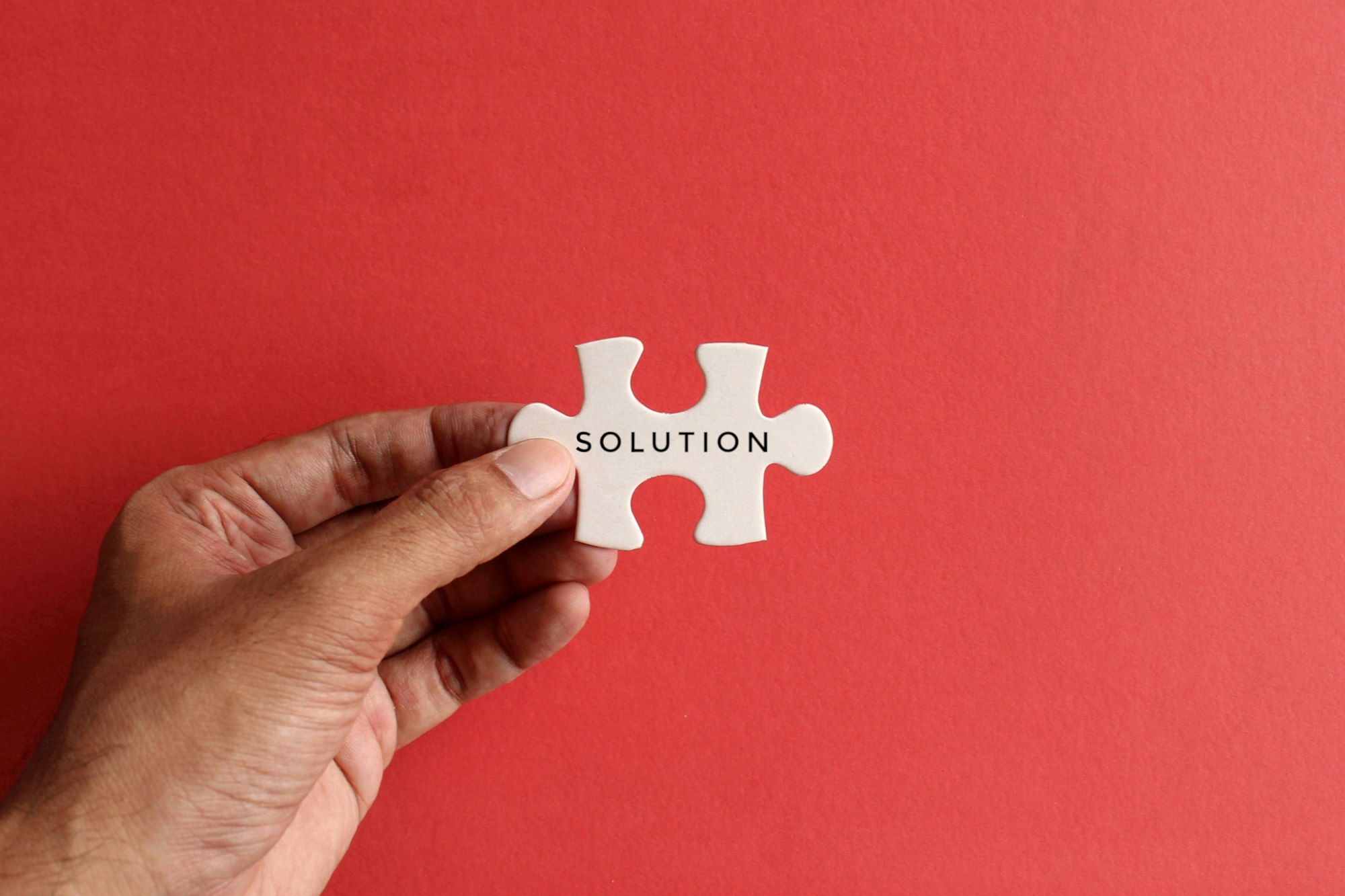 Hand holding puzzle pieces with text SOLUTION on red background