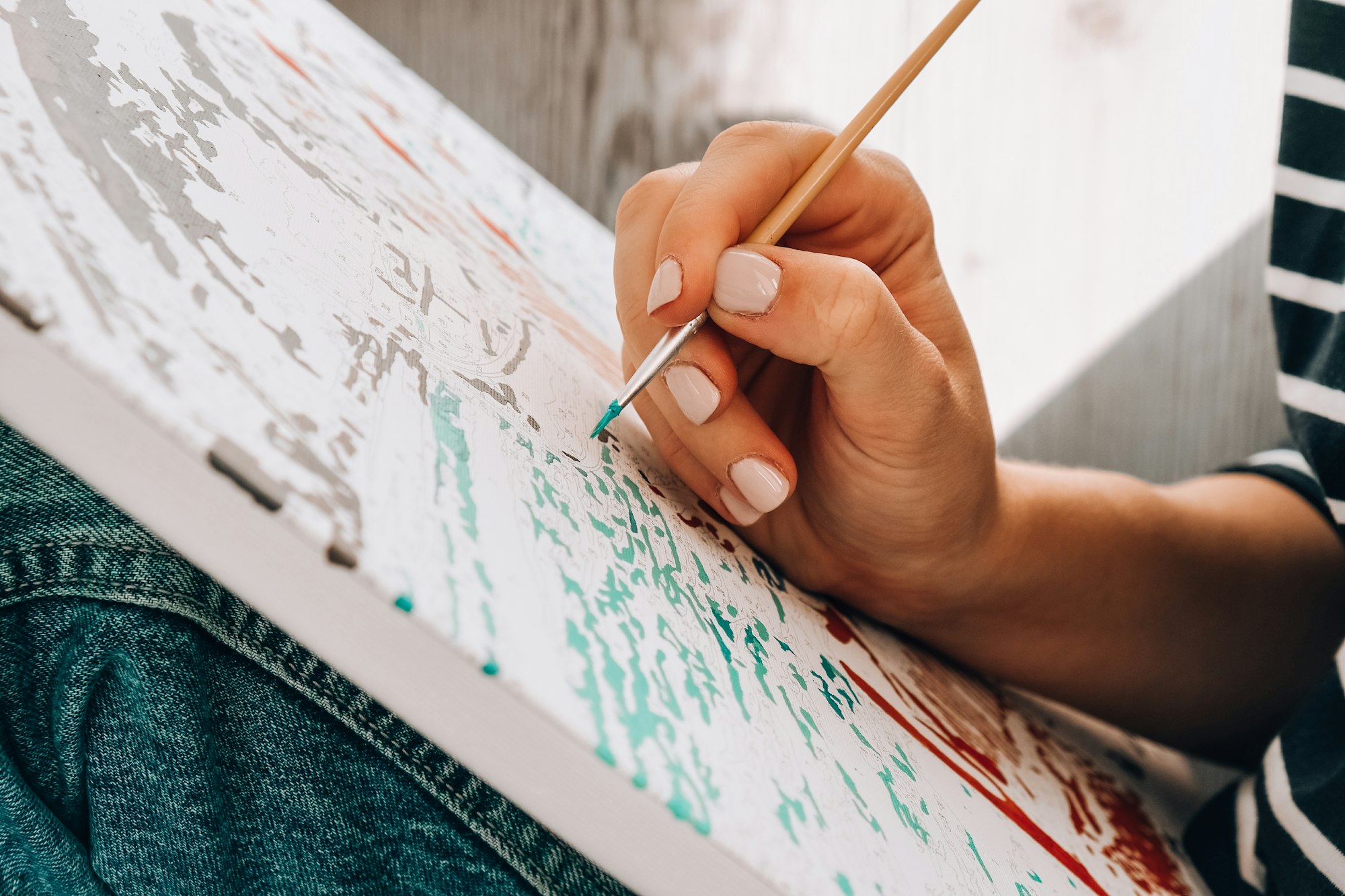 Painting on canvas by numbers and numbered jars of paint. Woman draws with a brush painting by numbe