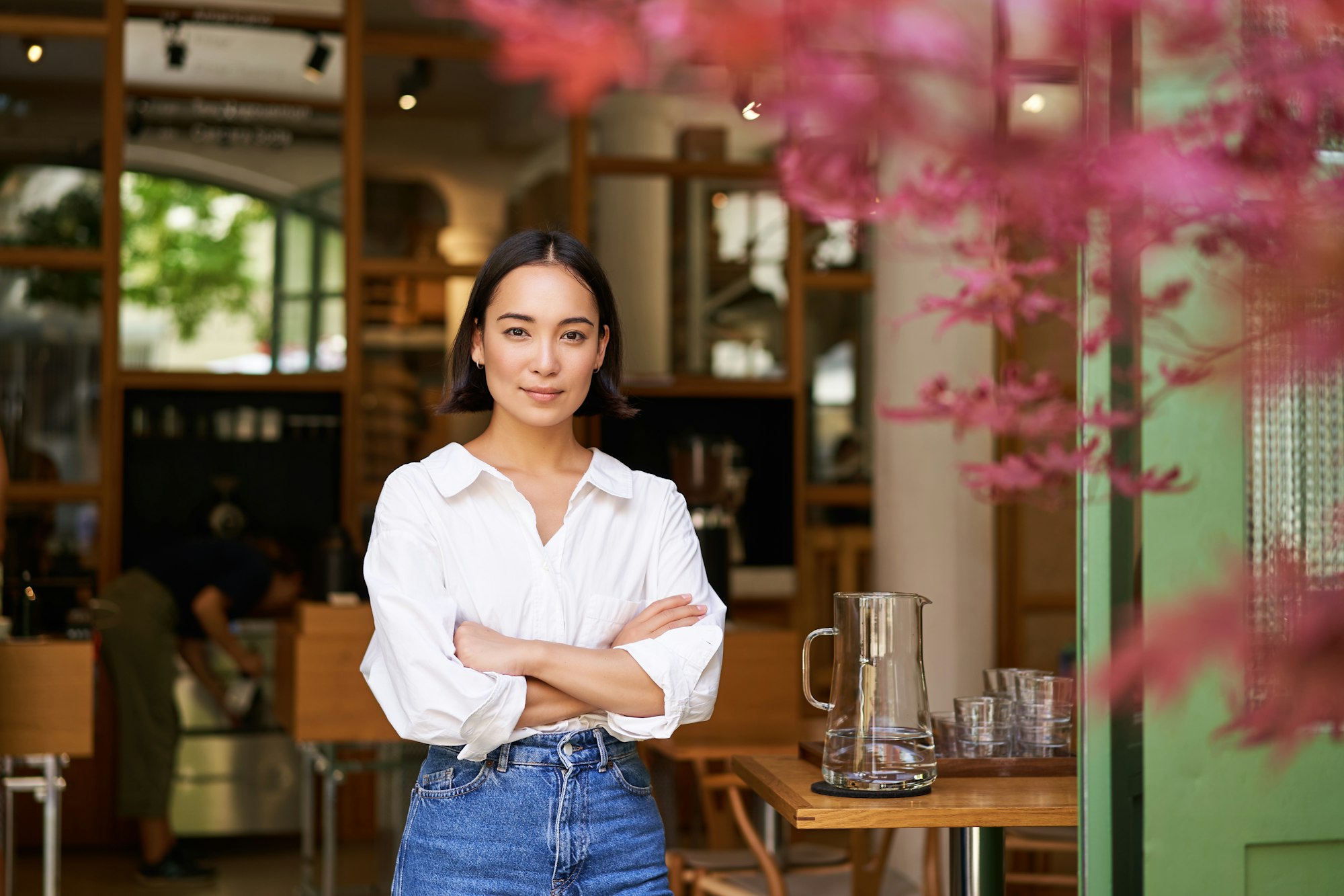 Portrait of young businesswoman in her own cafe, manager standing near entrance and inviting you