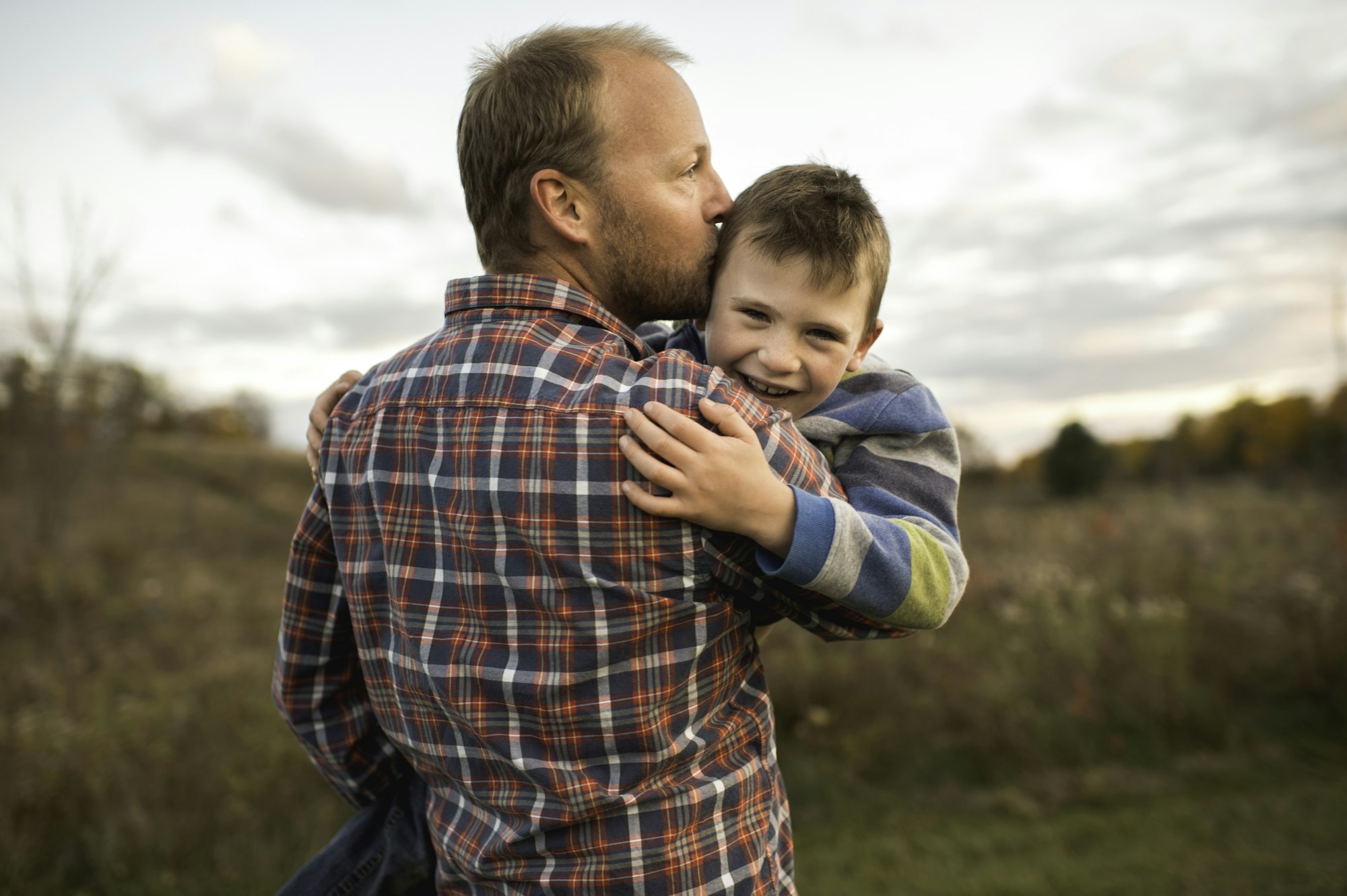 Rear view of father carrying smiling son, kissing him on forehead