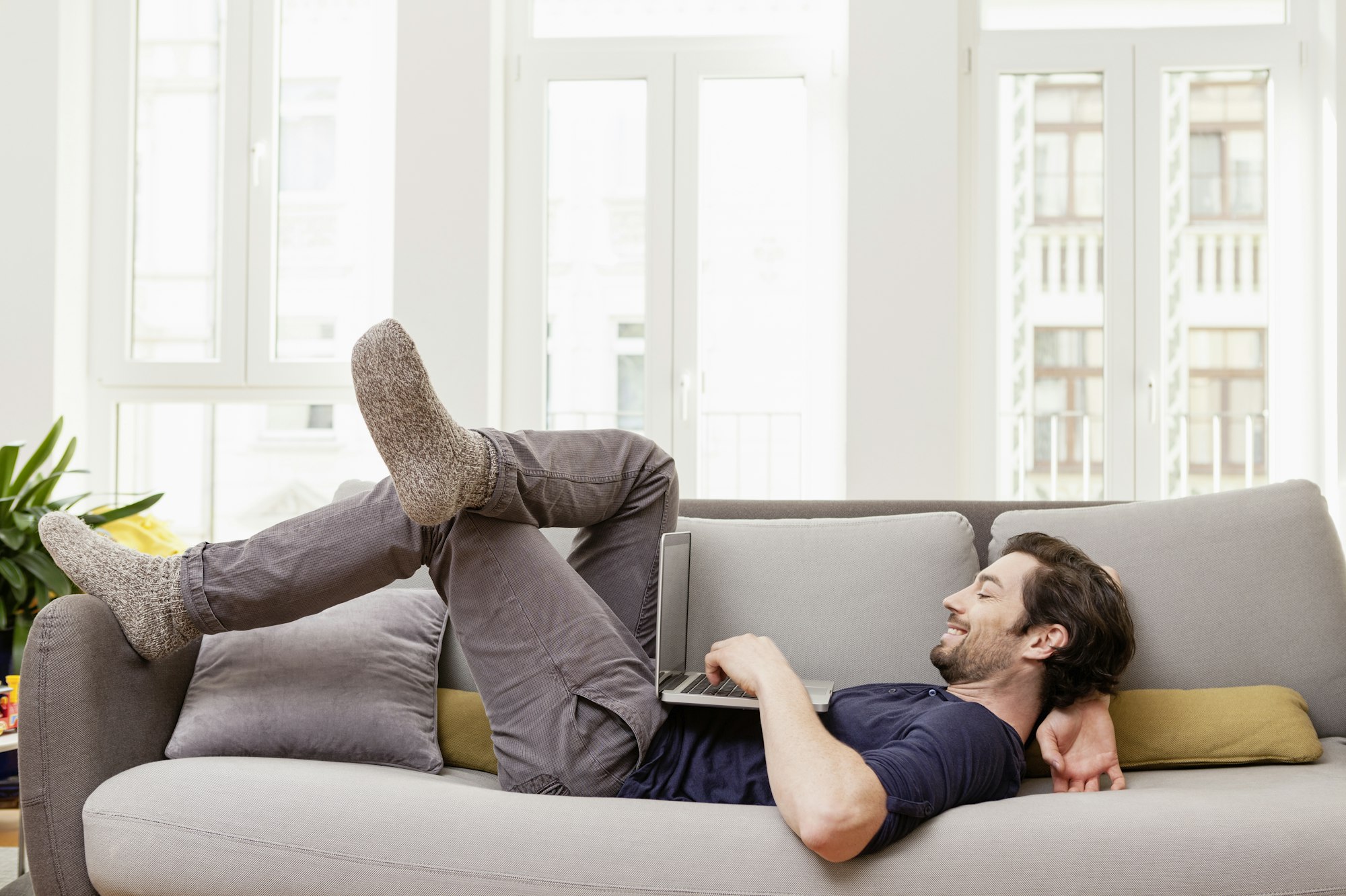 Relaxed man lying on couch using laptop