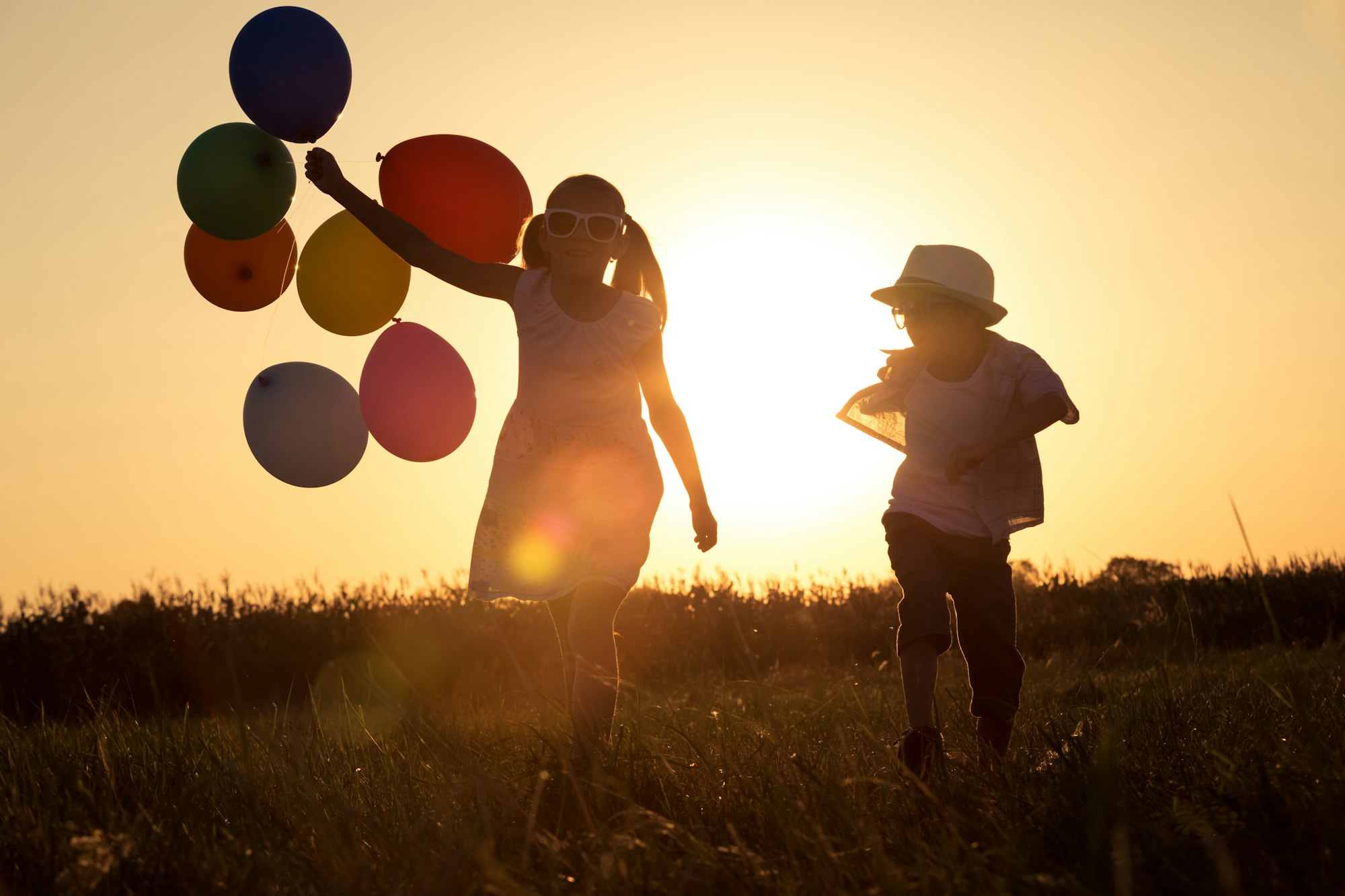 Silhouette of two happy children which playing on the field at t