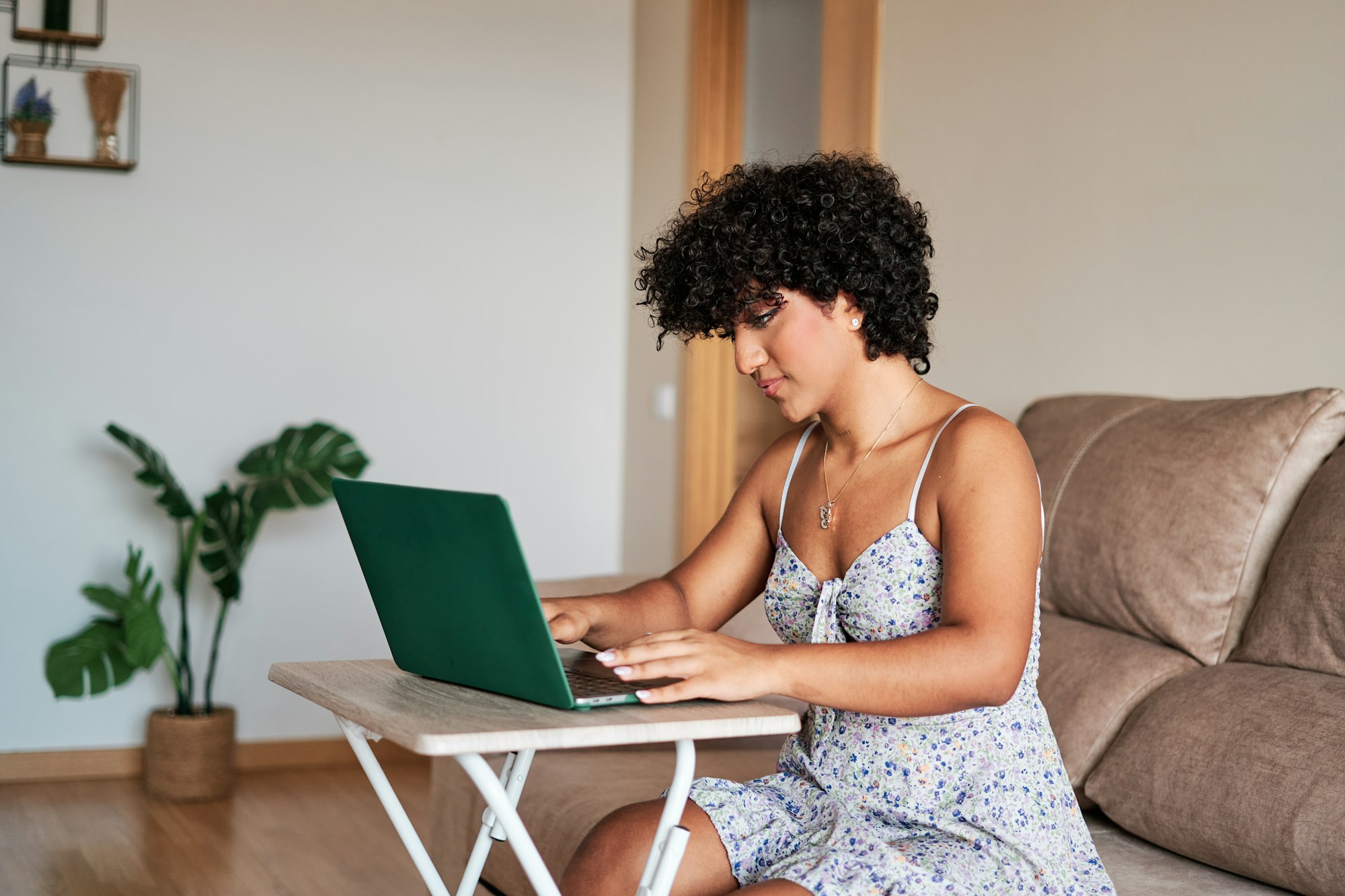 Transgender woman working with a laptop while sitting on a sofa in the living room at home.