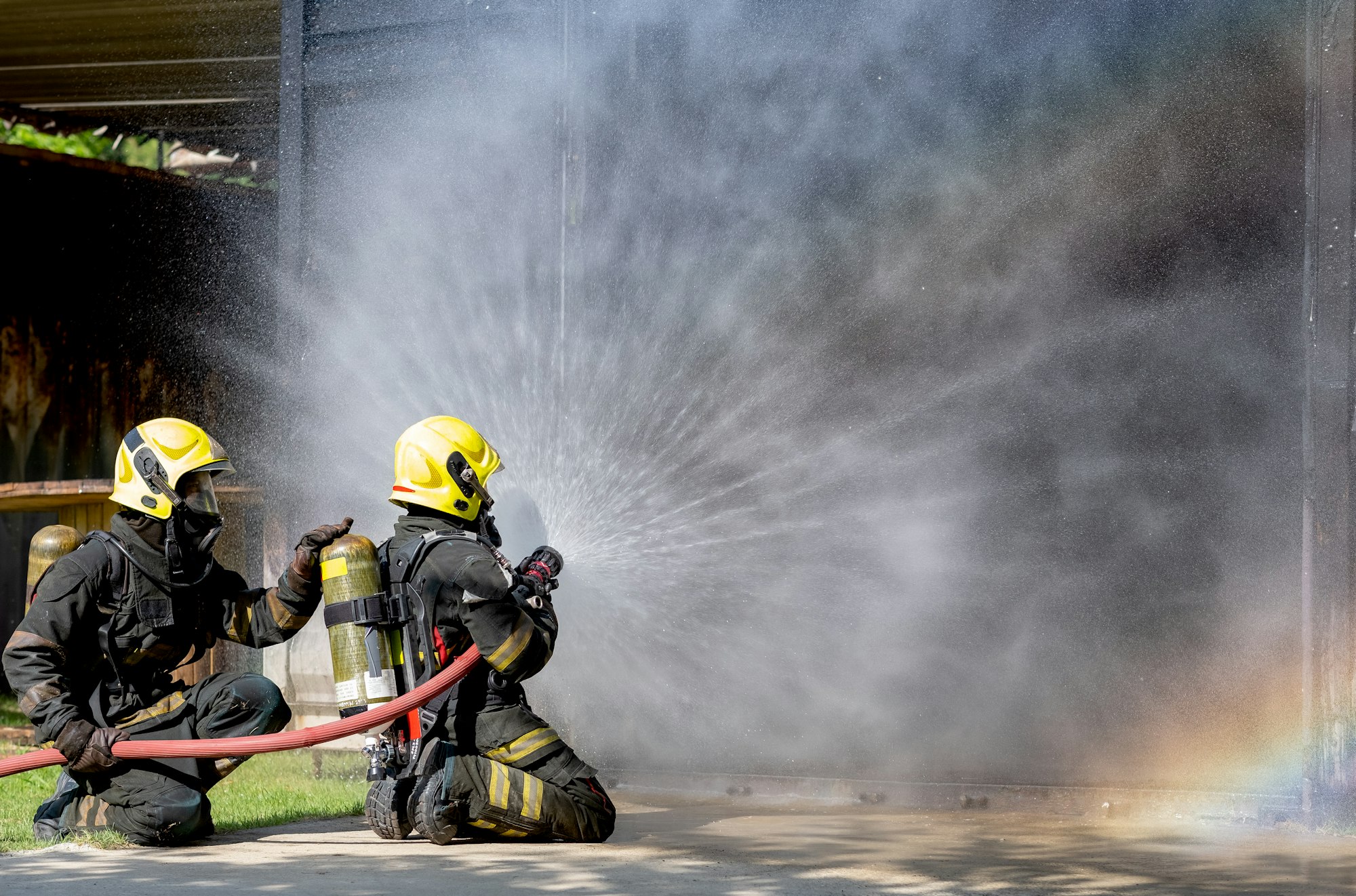 TTwo firefighters sit on floor and spray of water with curtain shape and rainbow reflex