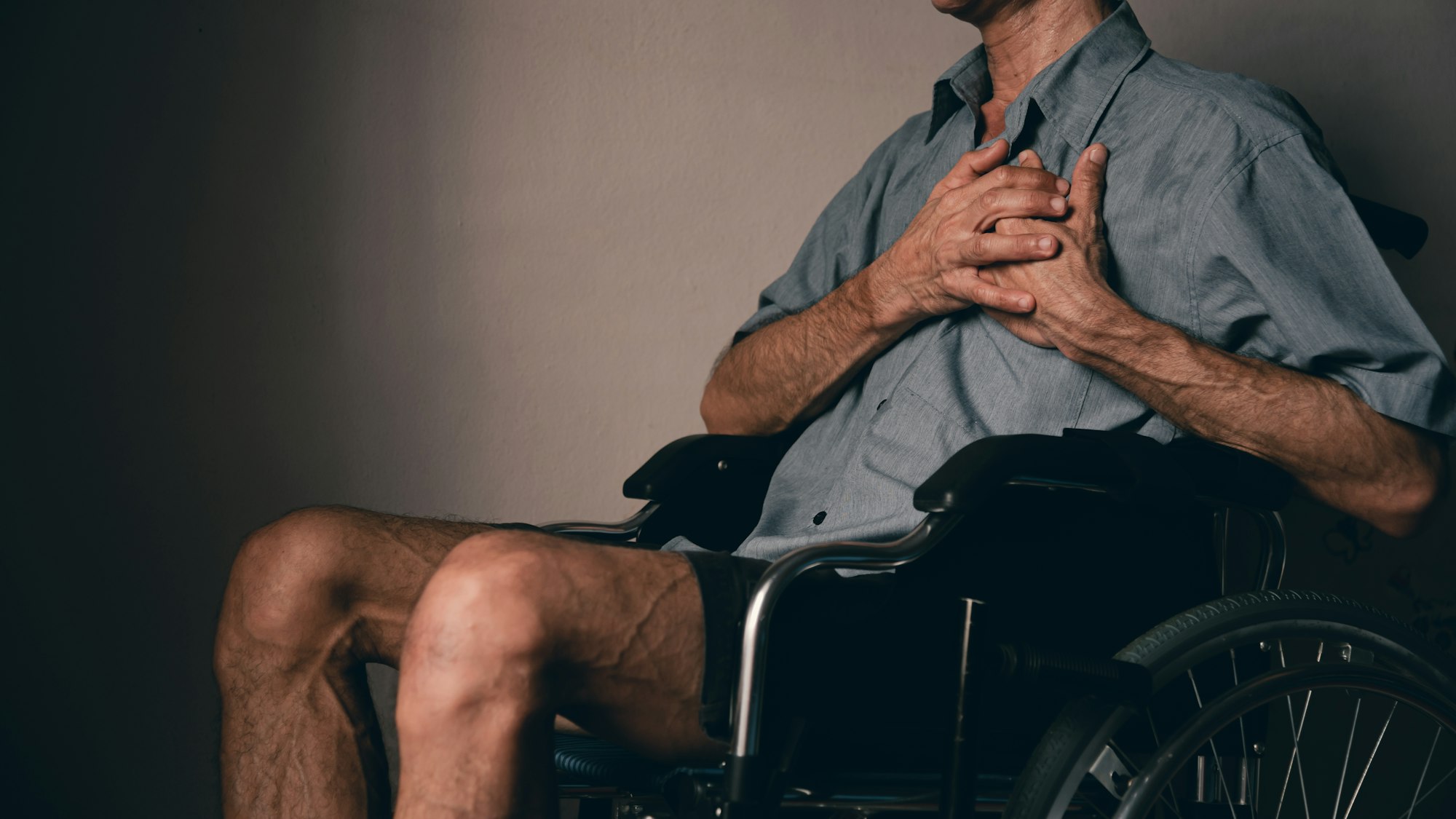 A handicapped man in a wheelchair holds his left chest due to heart disease pain.