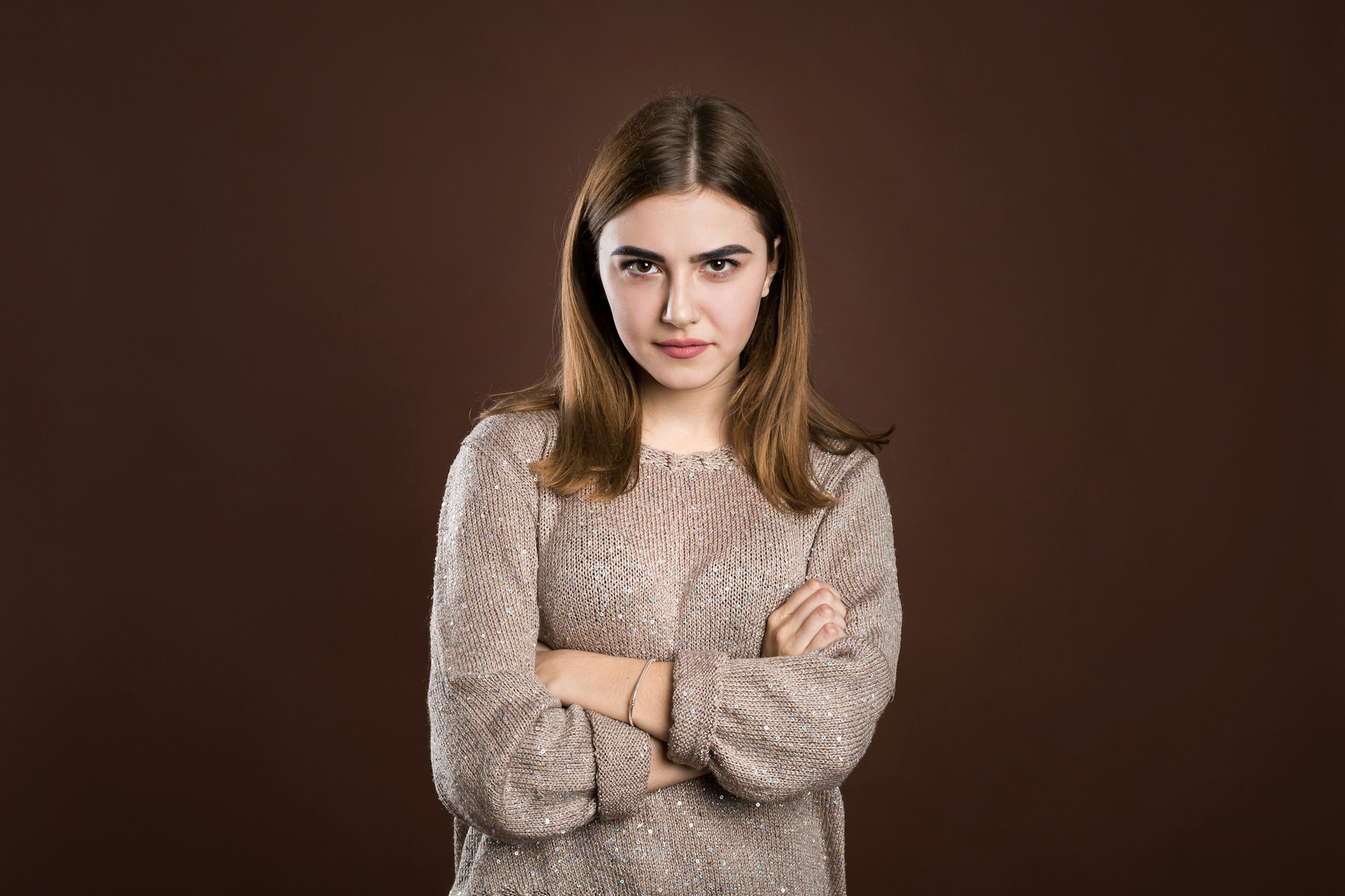 Girl frowning her face in displeasure, wearing loose long-sleeved sweater, keeping arms folded.