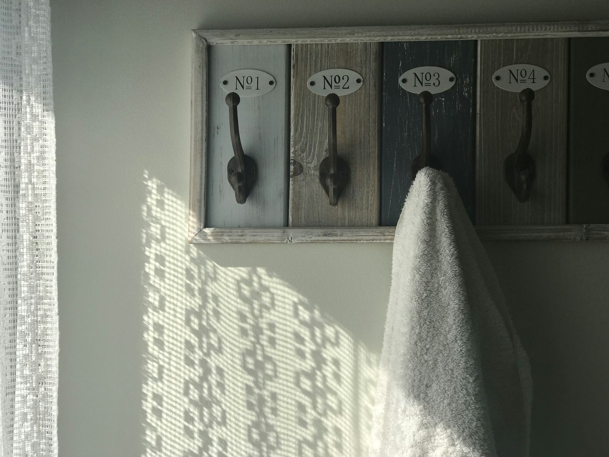 Light shines through the lace curtains in the bathroom where a towel is hung on the wall