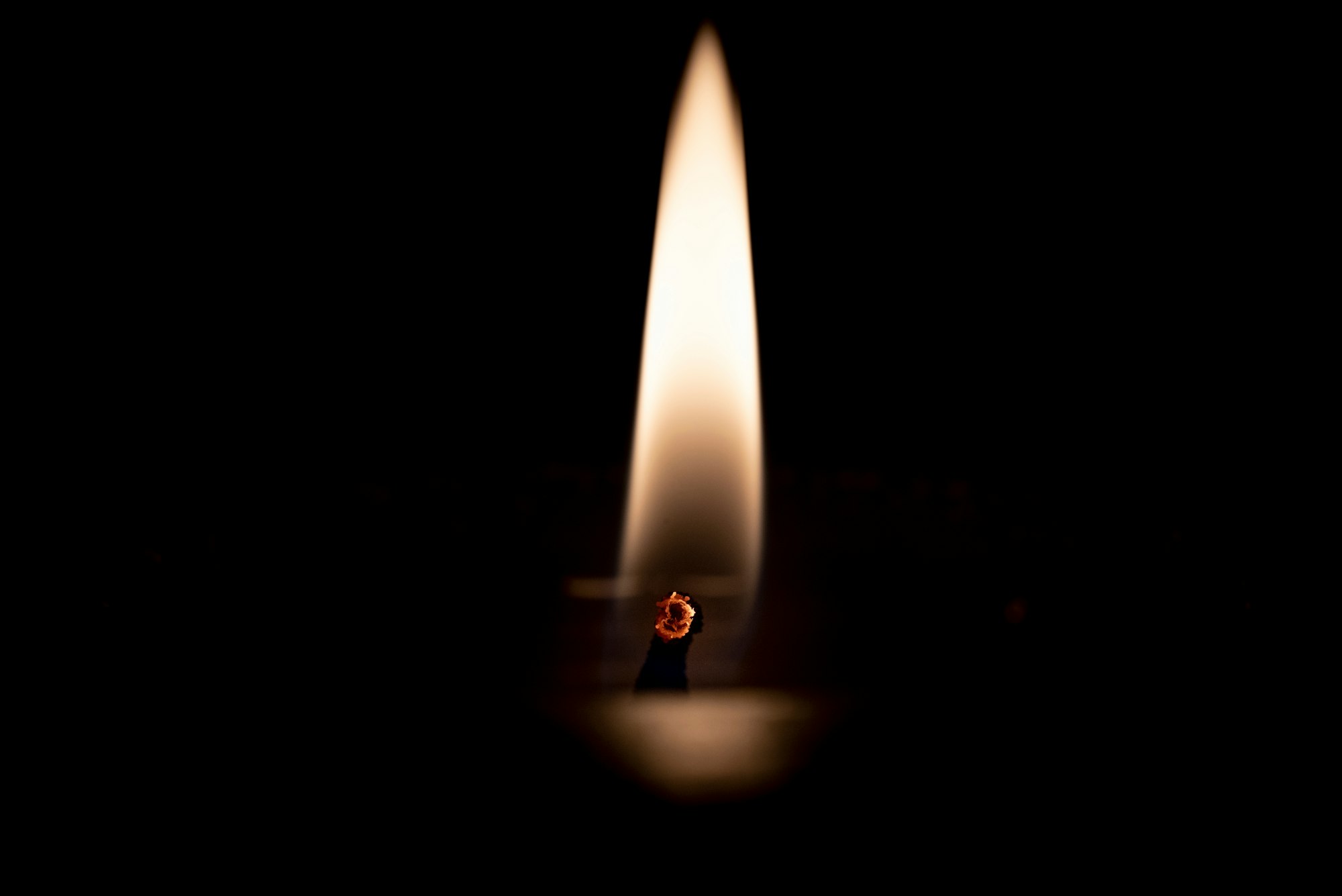 Macro close up of a flame from a single burning candle wick in dark night.